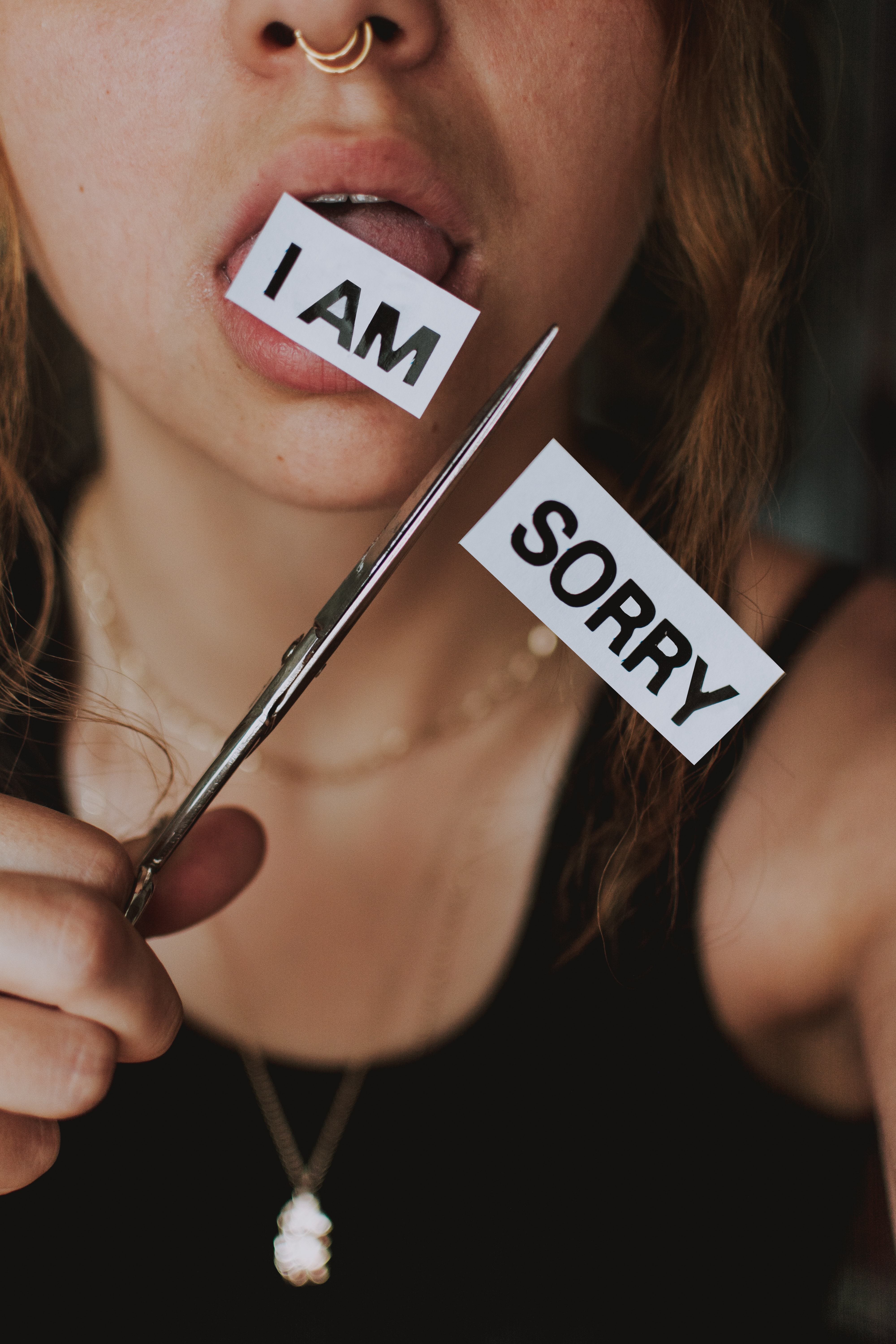 Adolescent woman with open mouth cutting off the "sorry" in "I am sorry" on a paper label. Only "I am" remains.