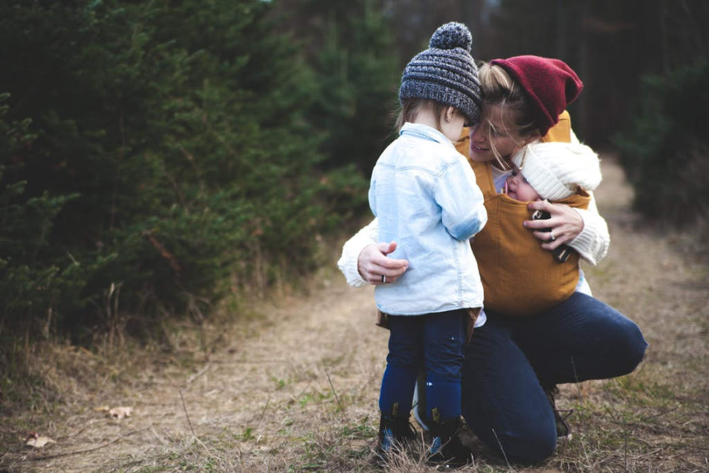 A mother in nature comforting her two small children and holding them close.