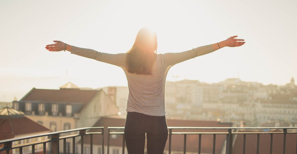 Woman standing on a balcony spreading her arms in freedom in sunshine.