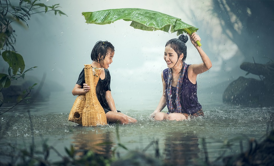 A mother and a daughter sitting in the rain soaking wet holding a palm leaf.