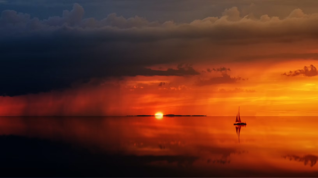 A single sailboat floats in still water during a beautiful sunset.