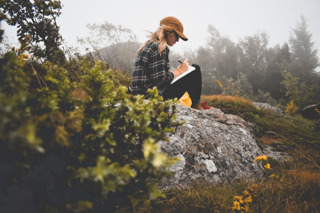 Woman sitting on a rock on a cloudy day writing something down in a journal.